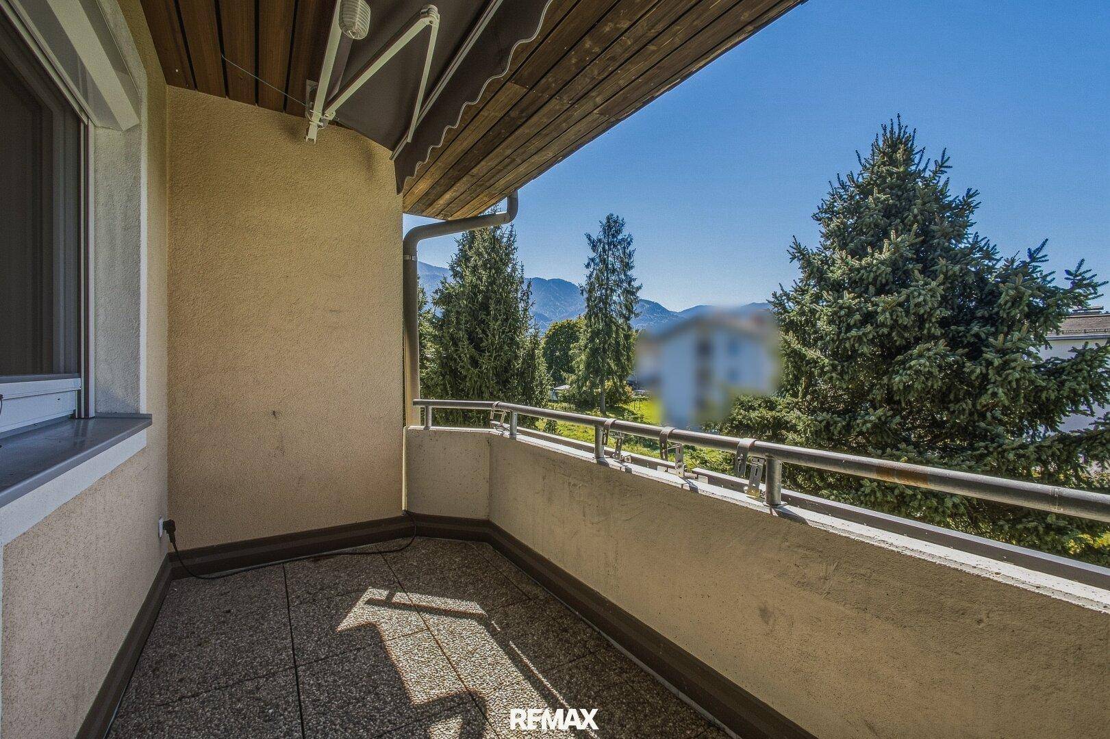 Sonniger Balkon mit Fliesenboden und Blick auf Bäume und Berge.
