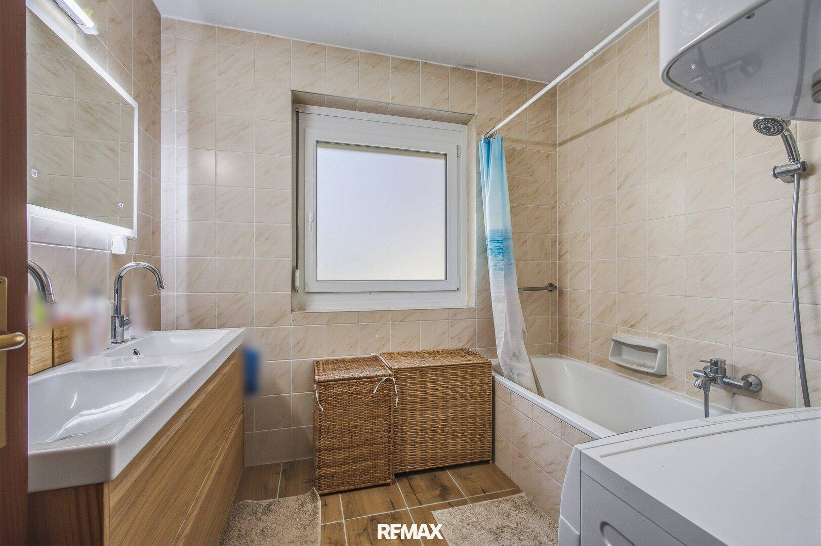 Gefliestes Badezimmer mit Badewanne, Einzelwaschbecken und Fenster.