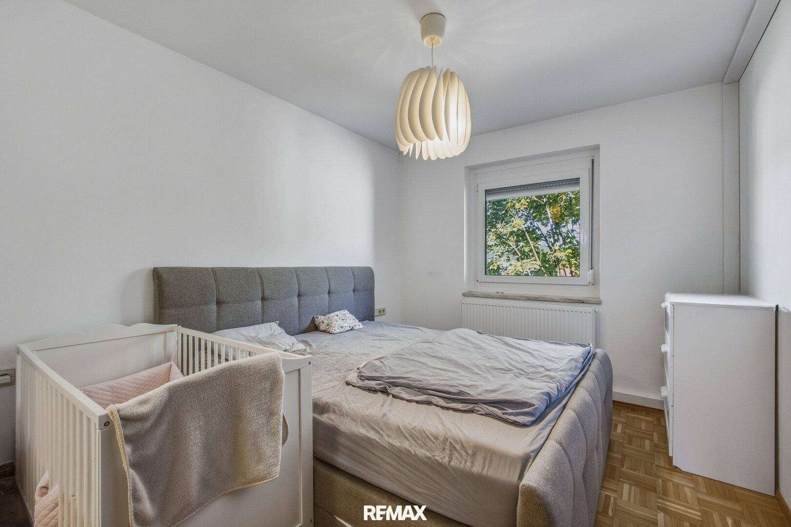 Helles Schlafzimmer mit Babybett, Doppelbett und Blick ins Grüne.