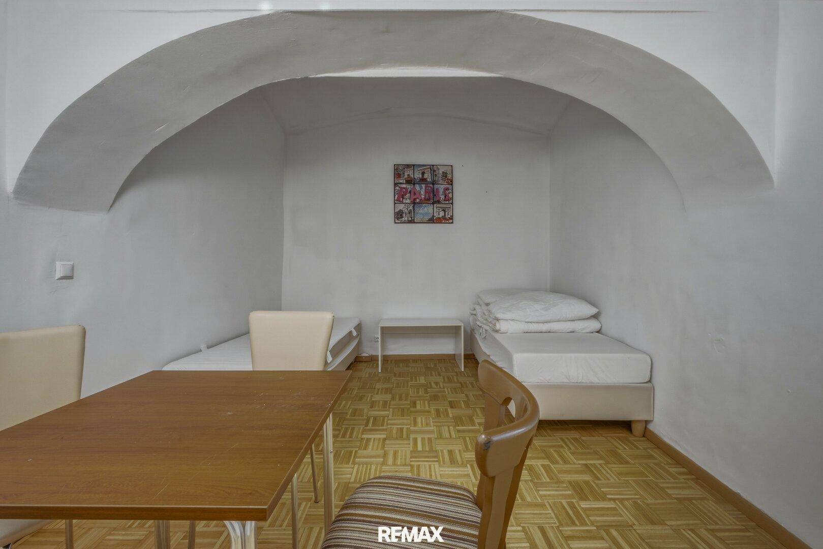 Schlafzimmer mit zwei Einzelbetten und einem Tisch unter einem gewölbten Deckenbogen.