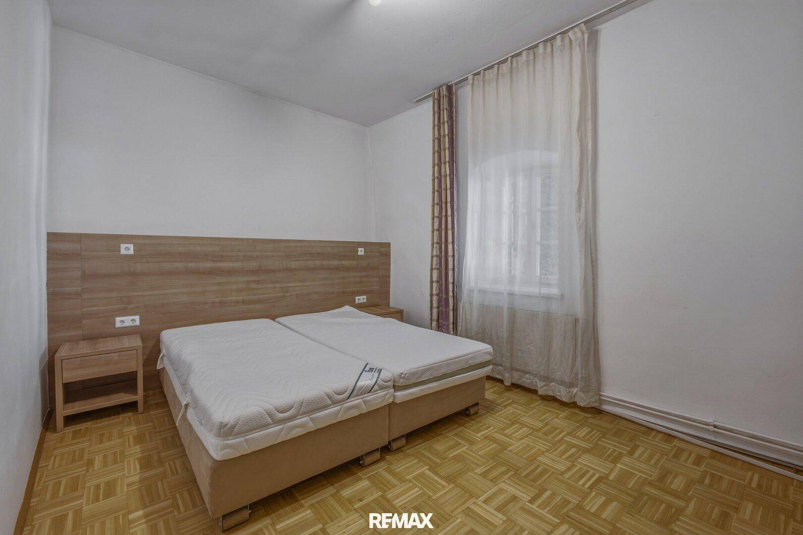 Schlafzimmer mit Doppelbett, Nachttischen und Vorhängen vor einem Fenster.