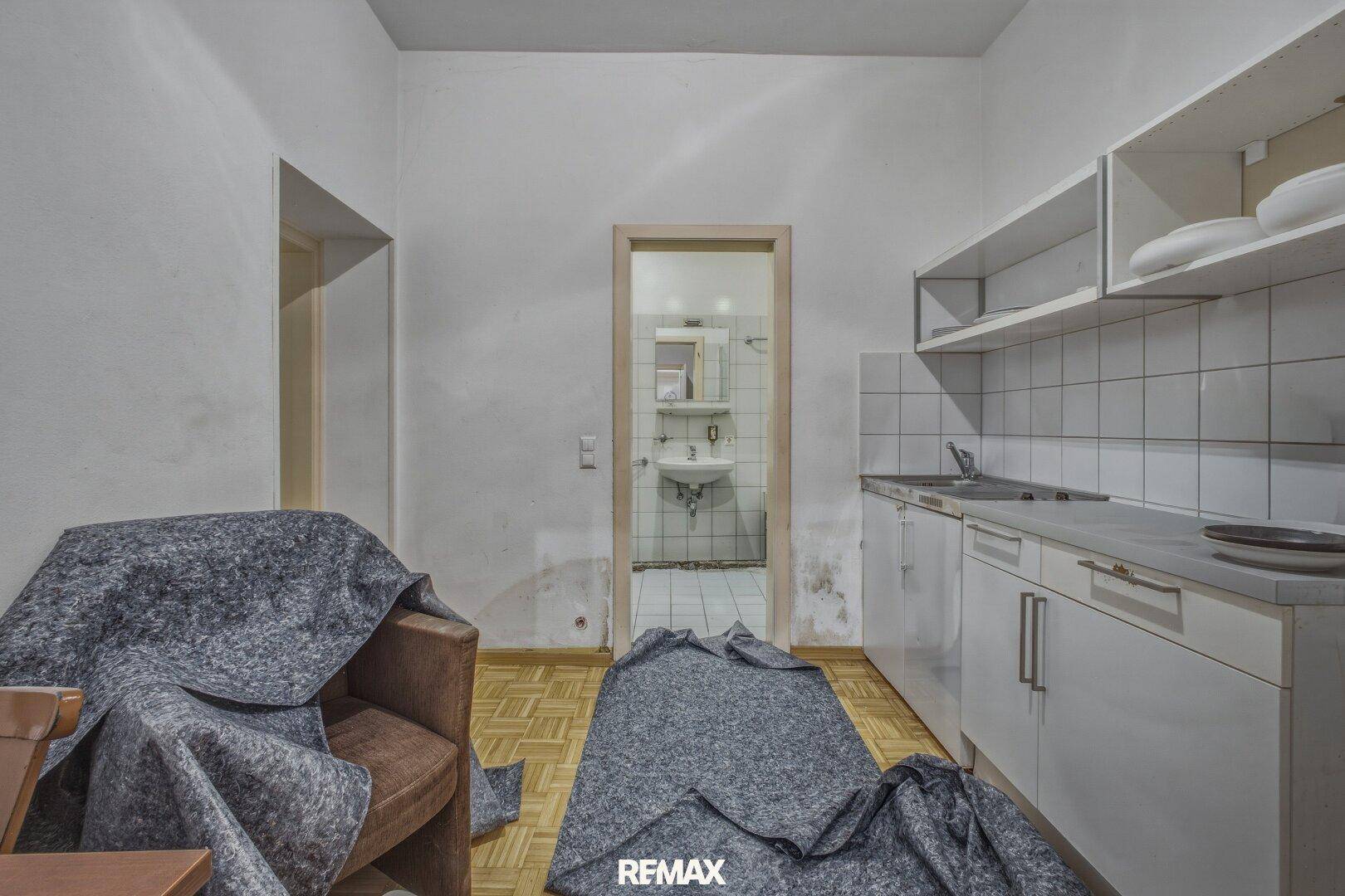 Küchenzeile mit Spüle und Schränken, Blick in ein angrenzendes Badezimmer.