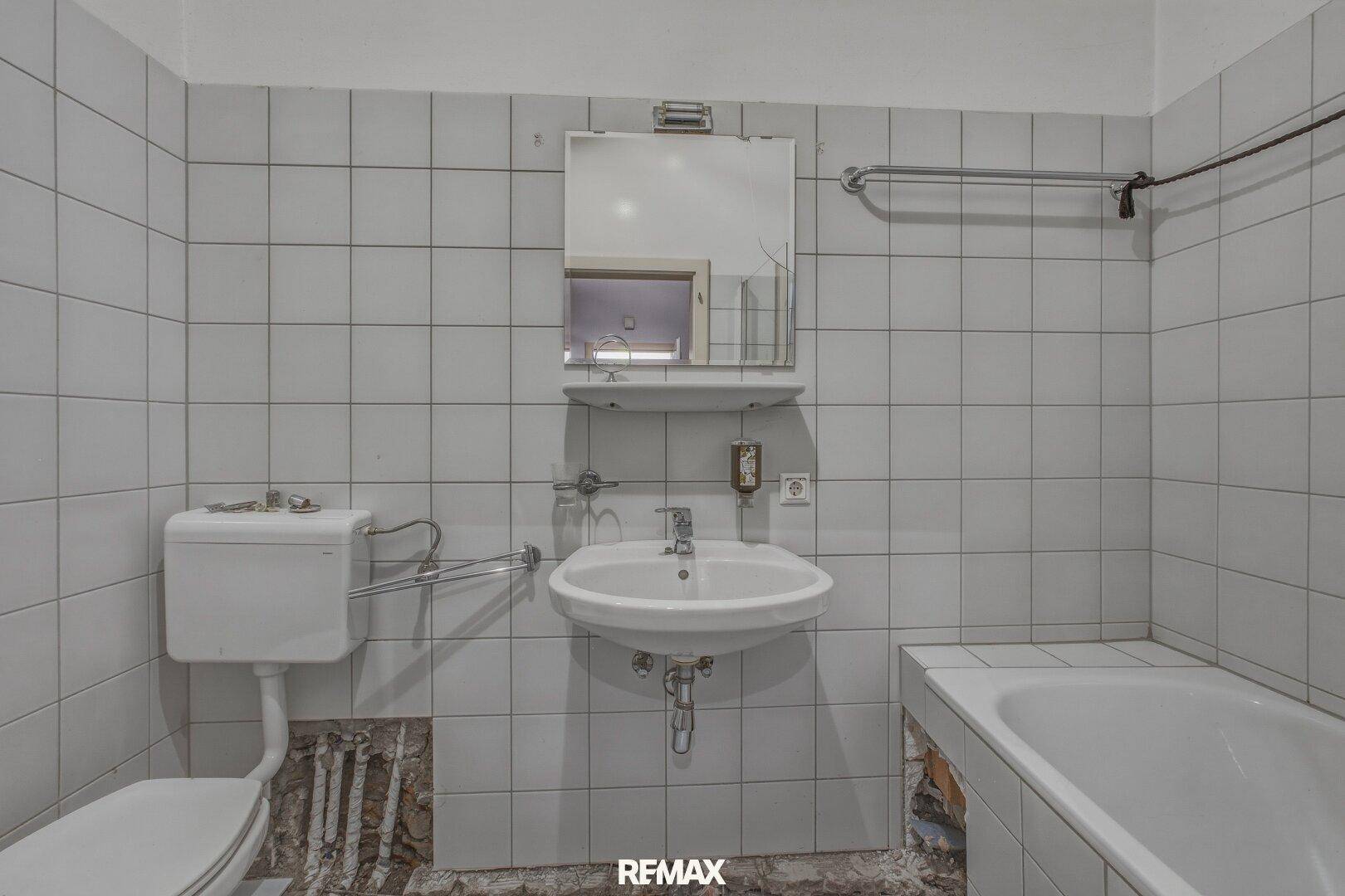 Badezimmer mit Waschbecken, Toilette und Badewanne, teilweise renovierungsbedürftig.