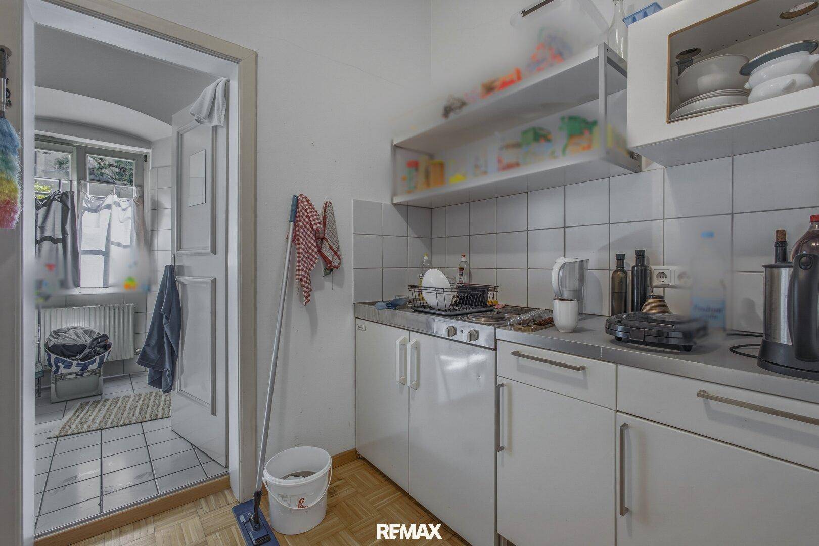 Kleine, voll ausgestattete Küchenzeile mit Spüle und Blick in ein Badezimmer.