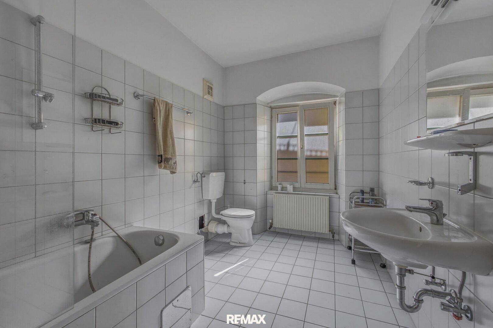Badezimmer mit Badewanne, Waschbecken und Toilette, gefliest in Weiß mit Fenster.