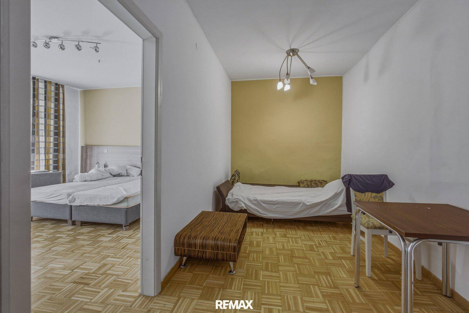 Schlafzimmer mit Bett und Tisch, angrenzend an einen weiteren Schlafbereich.