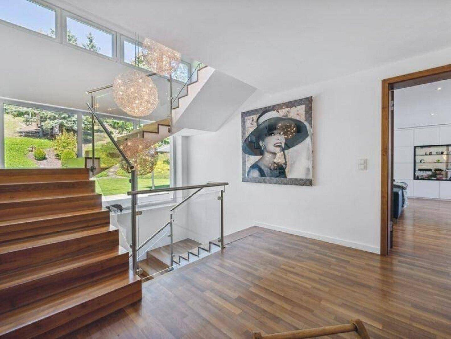 Moderner Eingangsbereich mit Holztreppe, Glasgeländer und großen Fenstern.