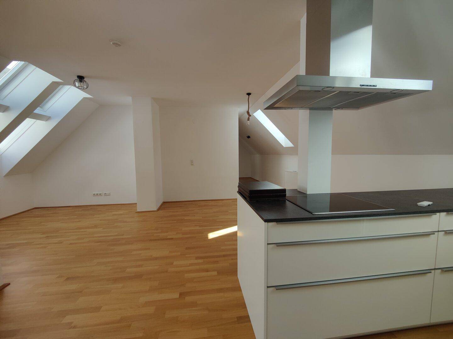 Moderne Küche mit Kochinsel, Induktionskochfeld und Dunstabzugshaube in einem hellen Dachgeschossraum.