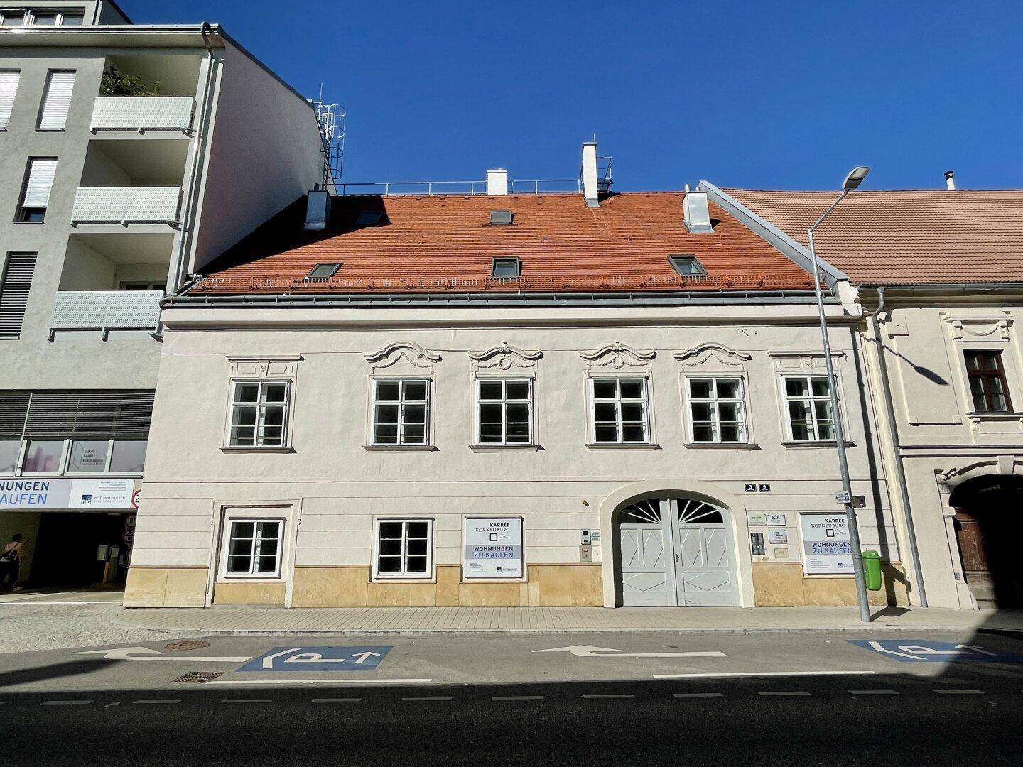 Historisches Wohnhaus mit traditioneller Fassade und roten Dachziegeln an einer Stadtstraße.