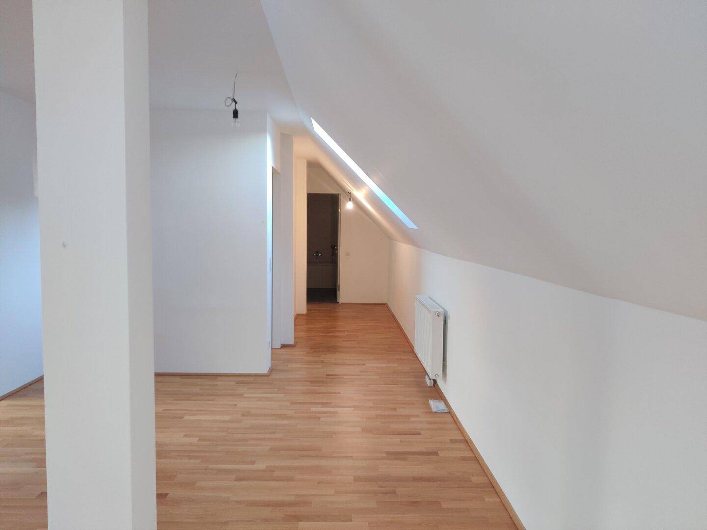 Heller Dachgeschossflur mit Parkettboden und Dachschrägen, der zu einem weiteren Raum führt.