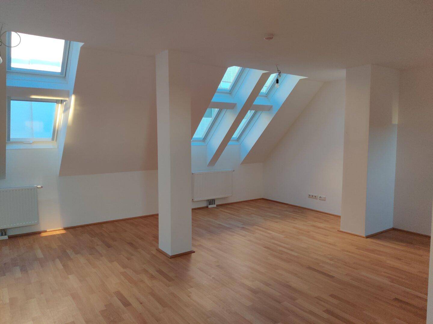 Lichtdurchfluteter Dachgeschossraum mit Parkettboden, hohen Decken und großen Dachfenstern.