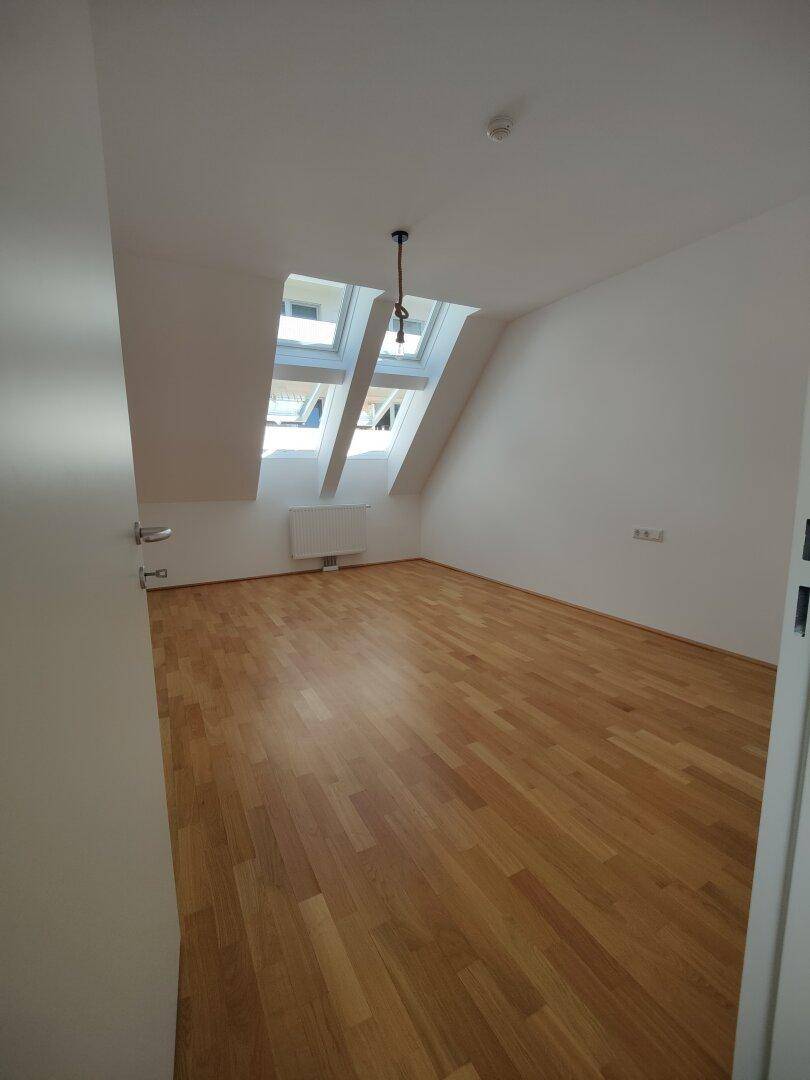 Helles Dachzimmer mit Parkettboden und schrägen Wänden, ideal als Schlaf- oder Arbeitszimmer.