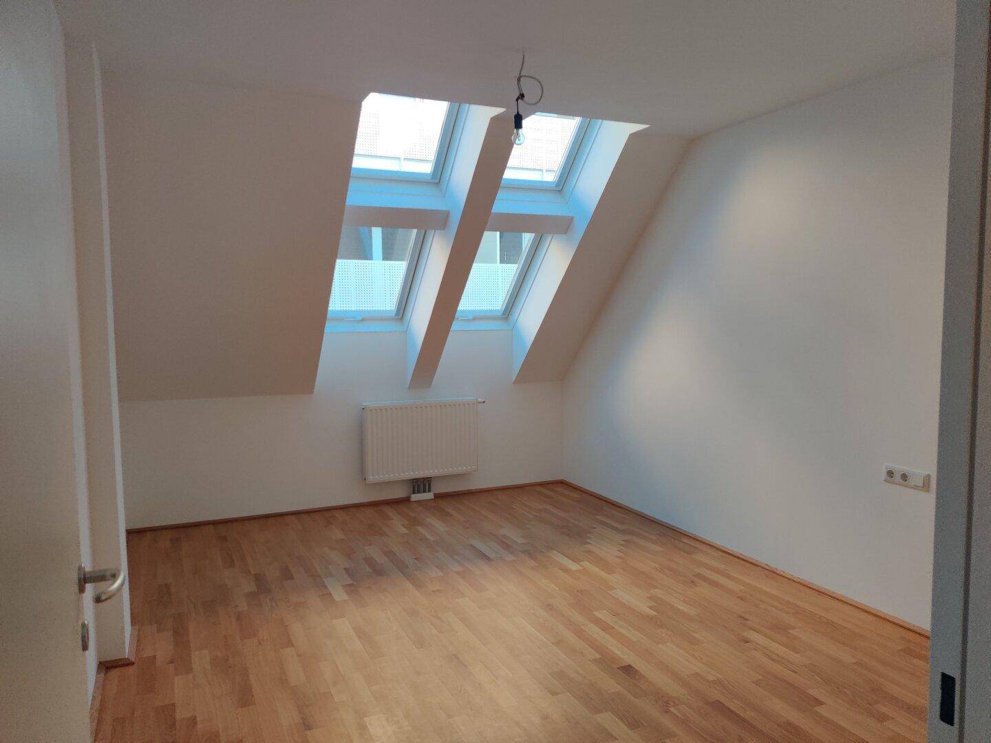 Geräumiges Dachzimmer mit Parkettboden und mehreren Dachfenstern, die viel Licht hereinlassen.