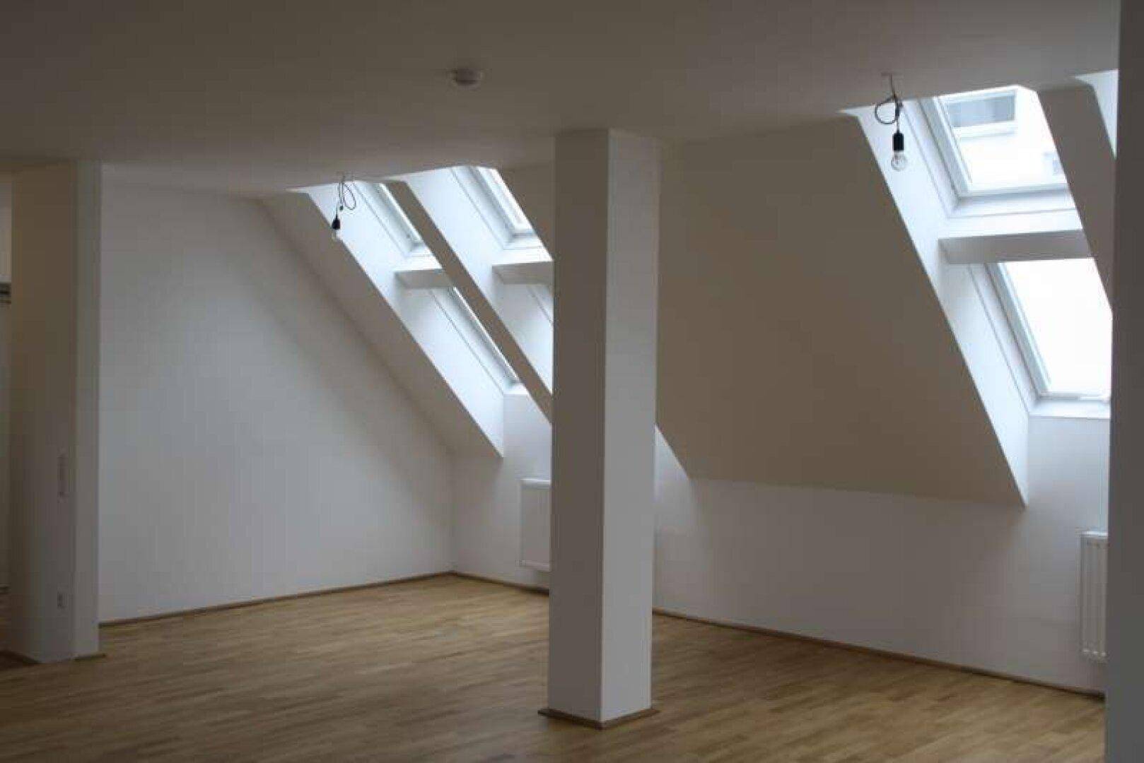 Großer Dachgeschossraum mit Parkettboden, Stützsäule und vielen Dachfenstern für Helligkeit.