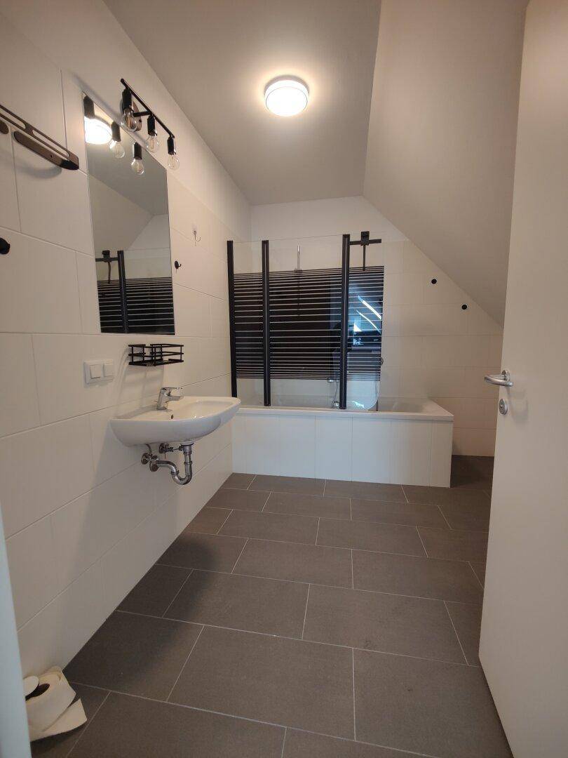 Modernes Badezimmer mit Badewanne, Waschbecken und dunklen Bodenfliesen im Dachgeschoss.