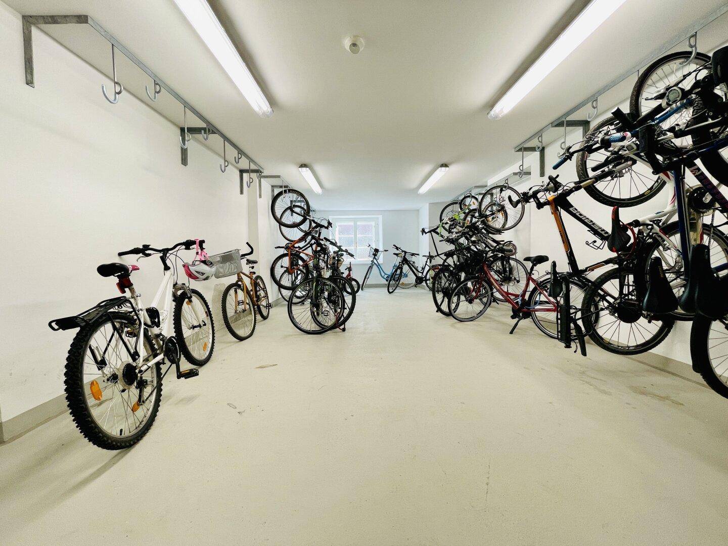 Geräumiger Fahrradraum mit vielen Fahrrädern und Aufhängemöglichkeiten an den Wänden.