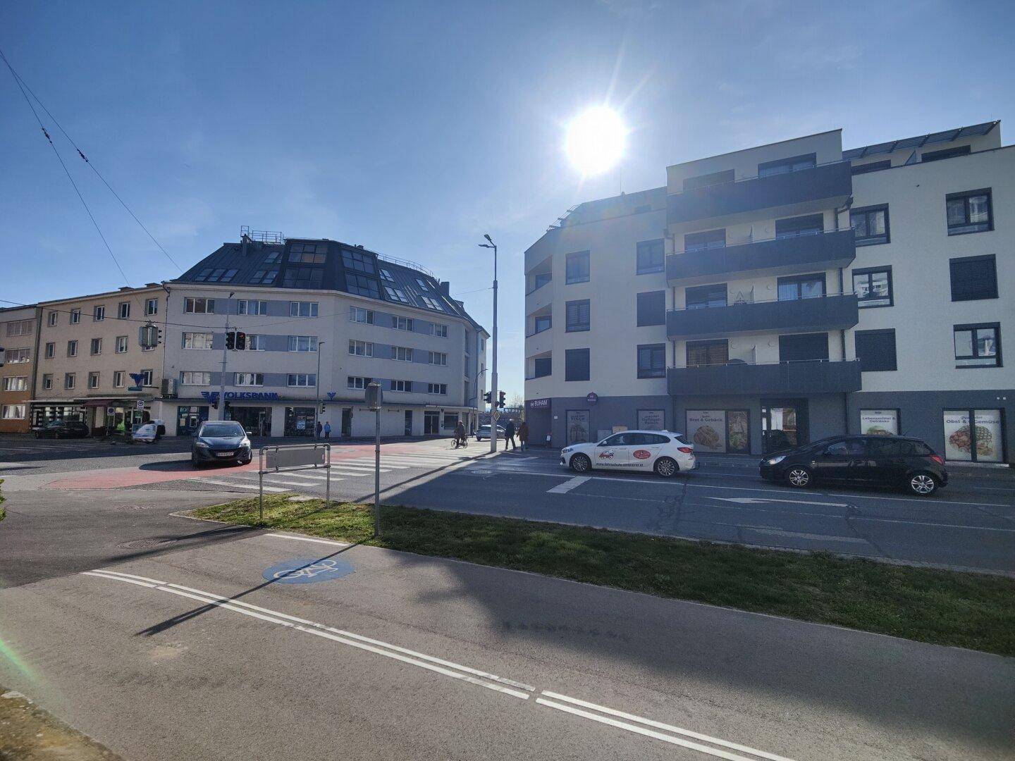 Straßenansicht eines modernen Wohngebäudes mit Geschäften im Erdgeschoss unter strahlend blauem Himmel.