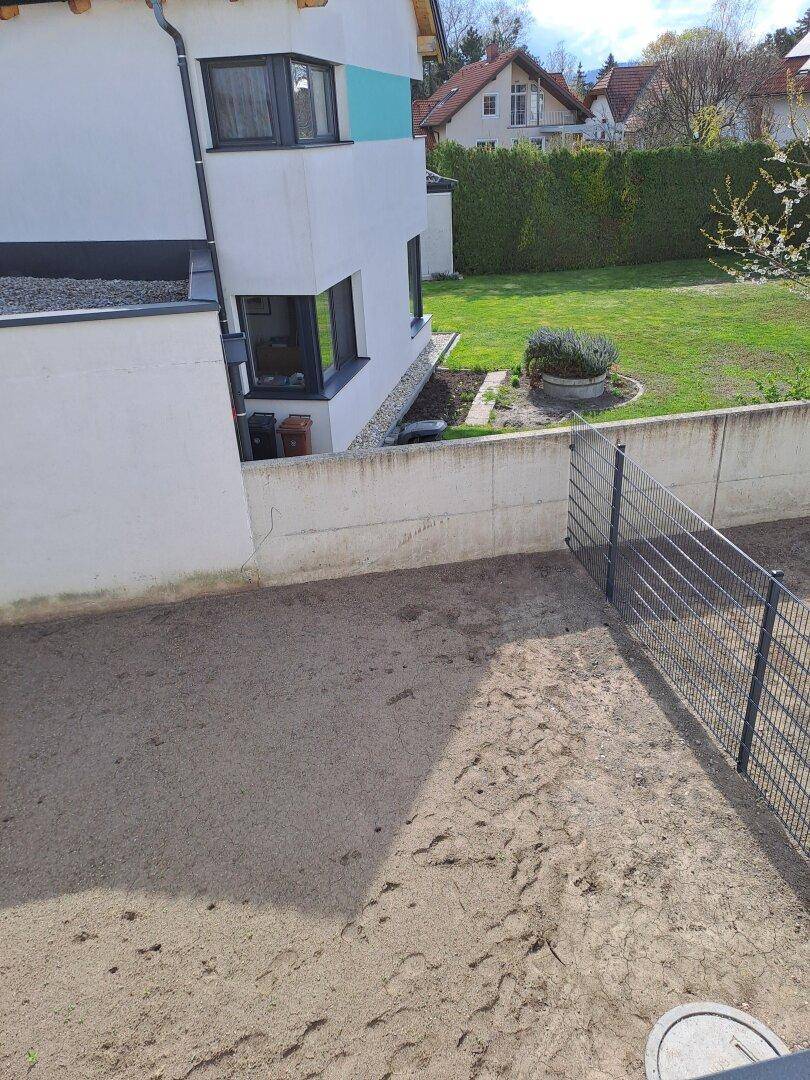 Unfertiger Gartenbereich mit Zaun und Blick auf die grüne Umgebung.
