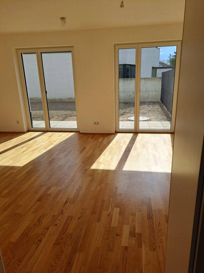 Geräumiger Raum mit Holzplankenboden und zwei Zugängen zum Gartenbereich.