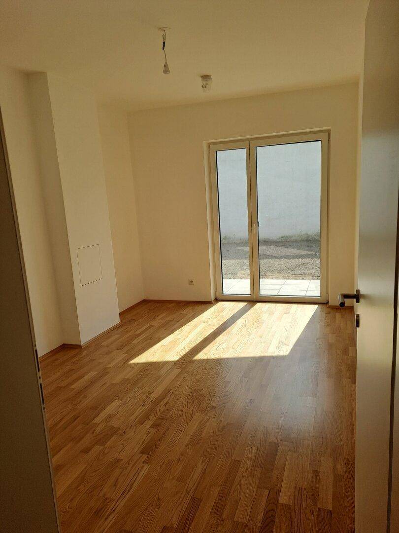 Sonniges Zimmer mit Holzplankenboden und Zugang zu einem Außenbereich.