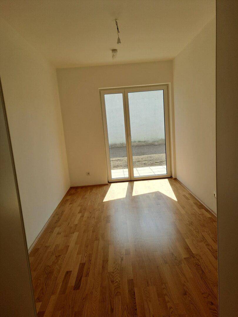 Helles Zimmer mit Holzplankenboden und viel Tageslicht durch die Terrassentür.