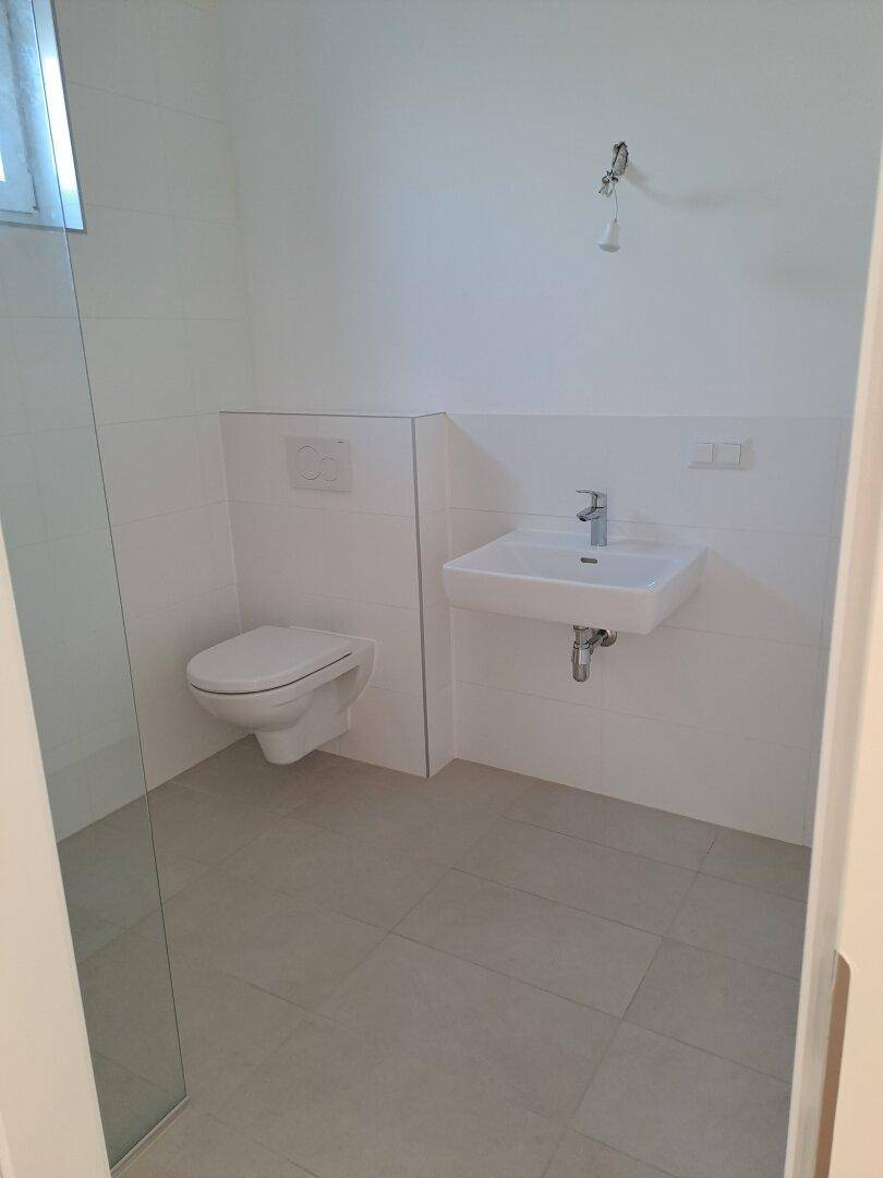 Modernes Badezimmer mit weißen Fliesen, wandhängendem WC und Einzelwaschbecken.
