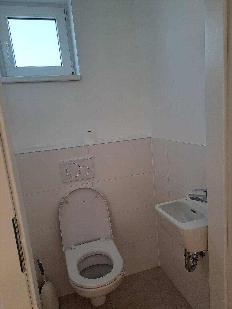 Gäste-WC mit wandhängendem WC, kleinem Waschbecken und Fenster.