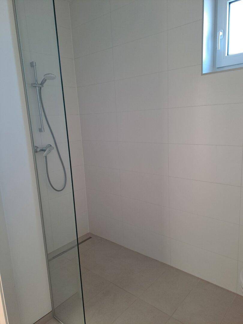 Großzügige begehbare Dusche mit weißen Fliesen und Fenster für Tageslicht.