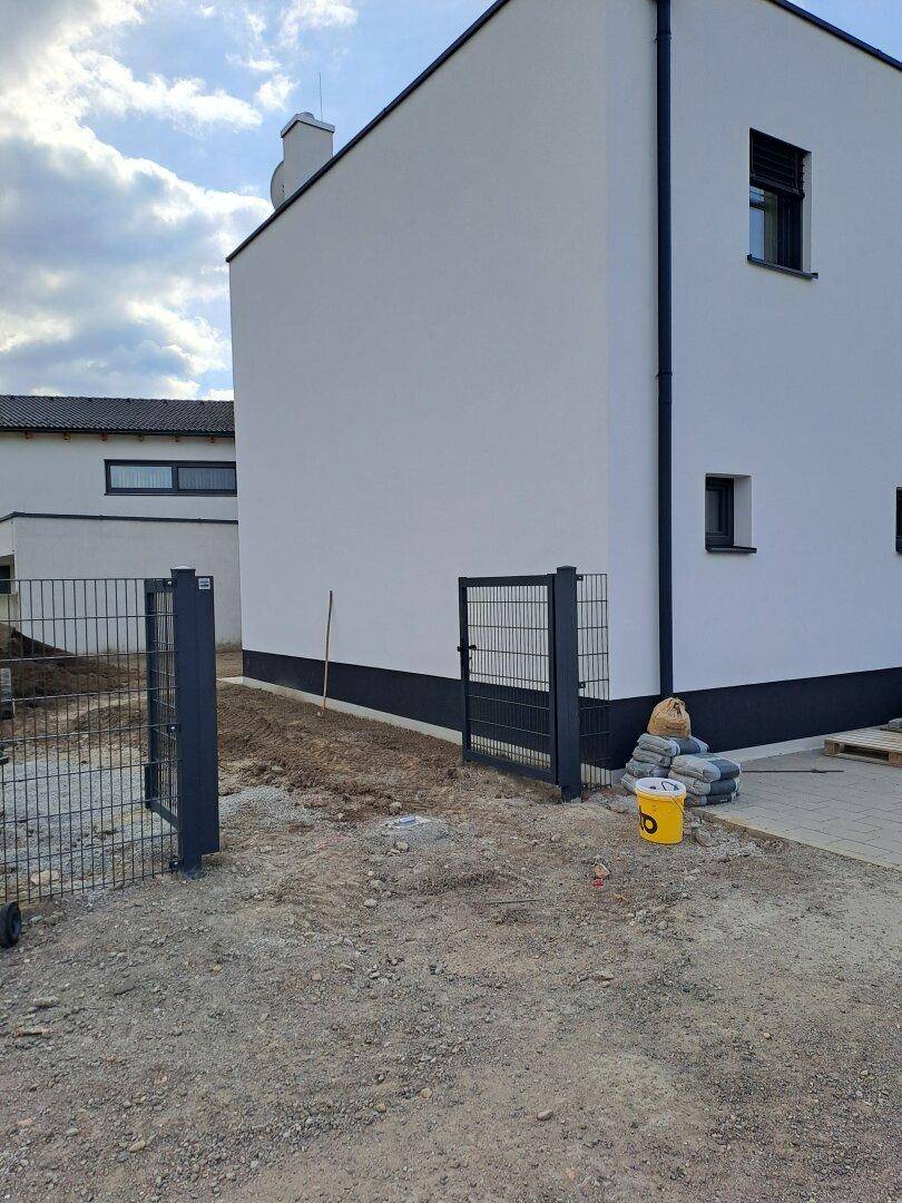 Außenansicht eines Neubaus mit moderner Fassade und unfertigem Eingangsbereich.
