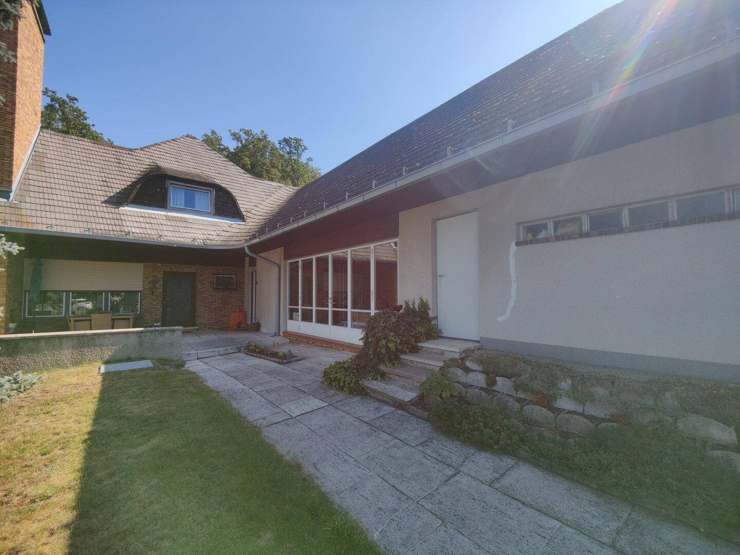 Seitenansicht des Hauses mit gepflastertem Weg, Rasenfläche und überdachtem Außenbereich.