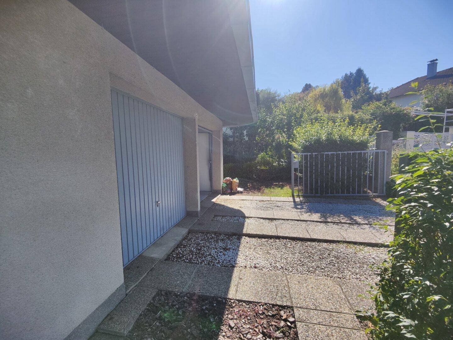 Garagenbereich mit hellblauen Toren, gepflastertem Vorplatz und Zugang zum Grundstück.