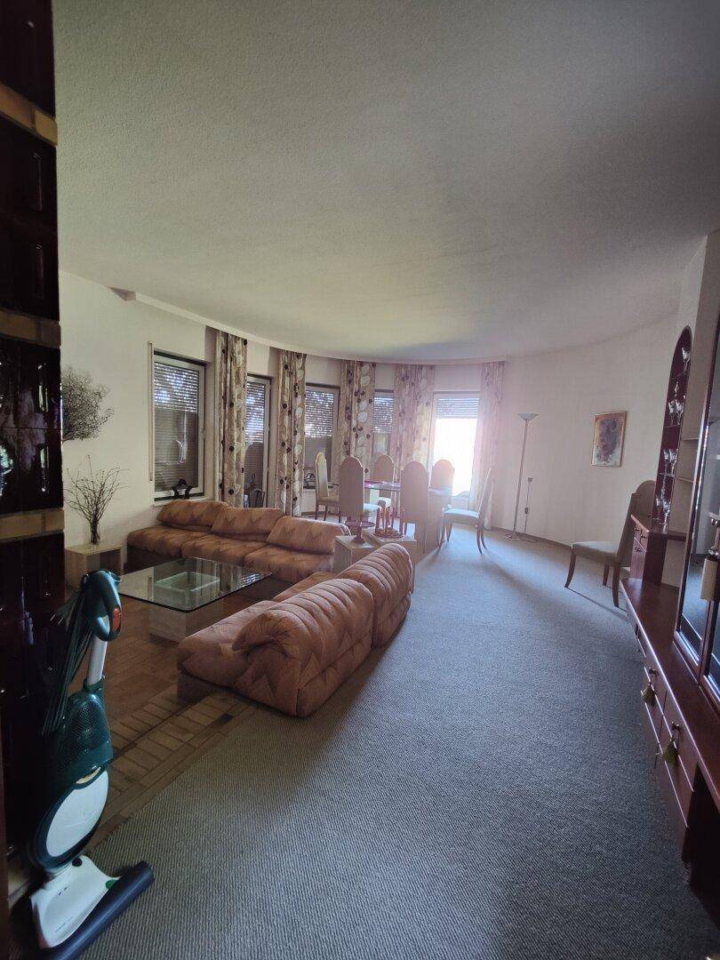 Großzügiger Wohn- und Essbereich mit Teppichboden, bequemen Sofas und vielen Fenstern.
