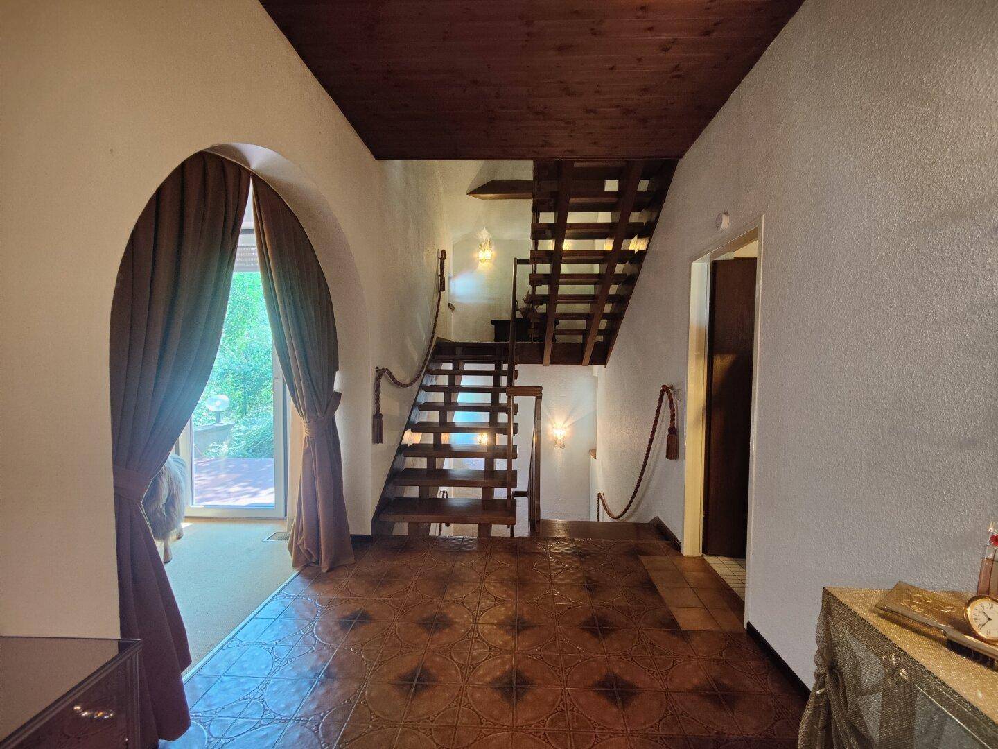 Eingangsbereich mit Holztreppe, gemusterten Fliesen und einem eleganten Rundbogen.