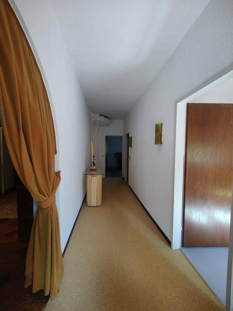 Heller Flur mit Teppichboden, weißen Wänden und einer Holztür am Ende.