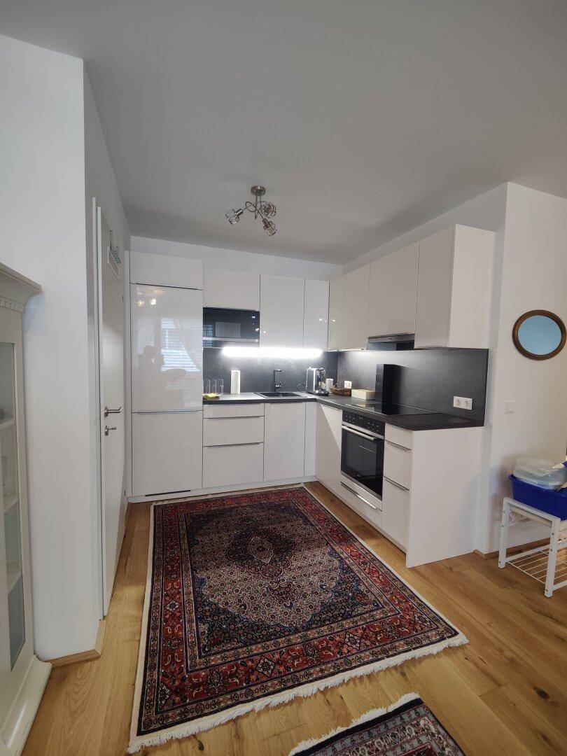 Moderne Küche mit weißen Hochglanzfronten, integrierten Geräten und Holzboden.