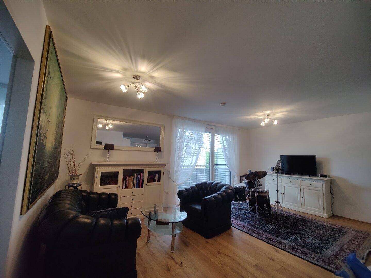 Geräumiges Wohnzimmer mit Holzboden, großem Spiegel und Blick auf den Balkon.