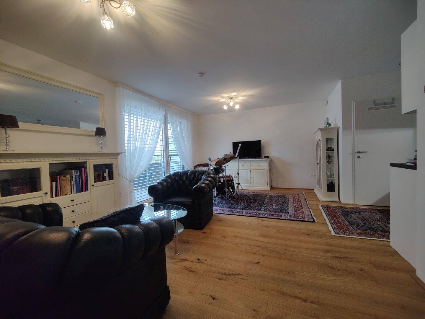 Heller Wohnbereich mit Holzboden, gemütlichen Ledersesseln und Zugang zum Balkon.