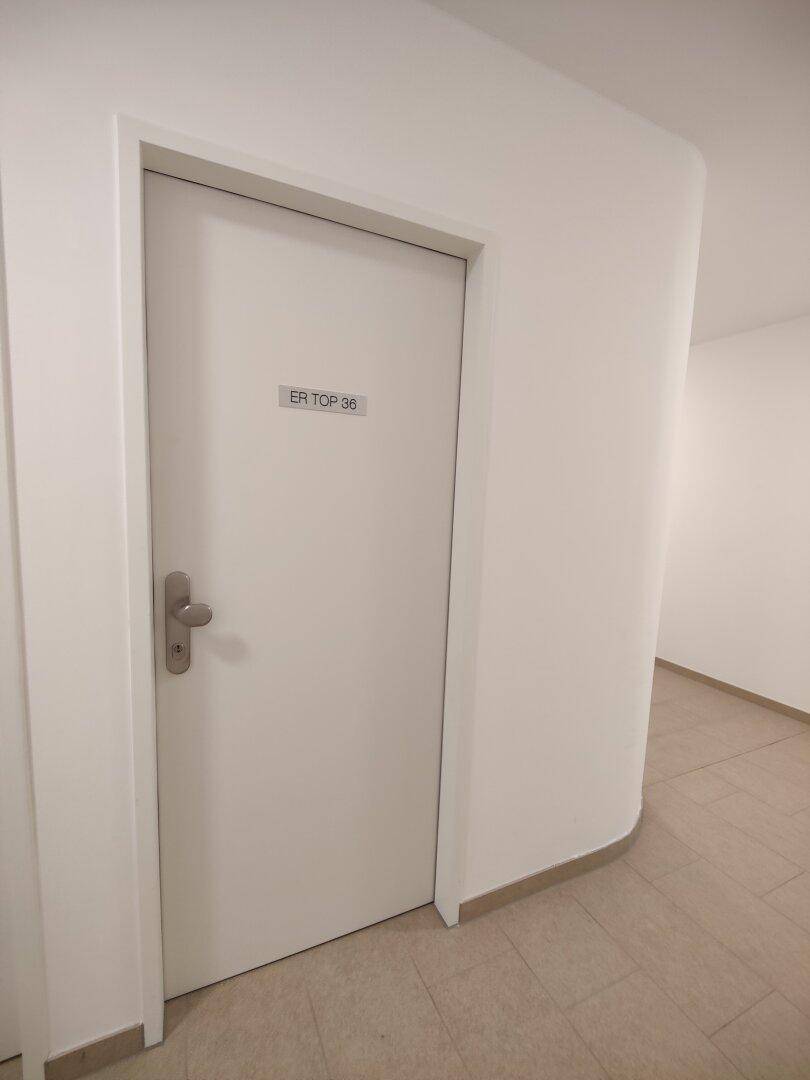 Eingangstür einer Wohnung in einem hellen Flur mit Fliesenboden.