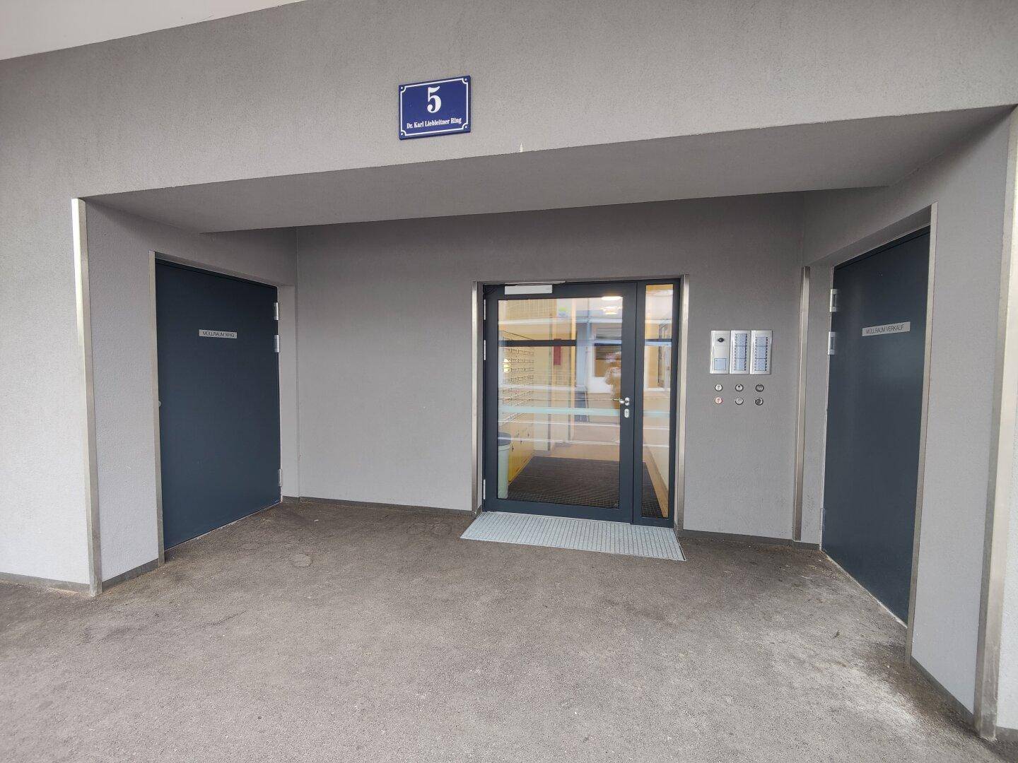 Moderner Gebäudeeingang mit Glasportal und Gegensprechanlage.
