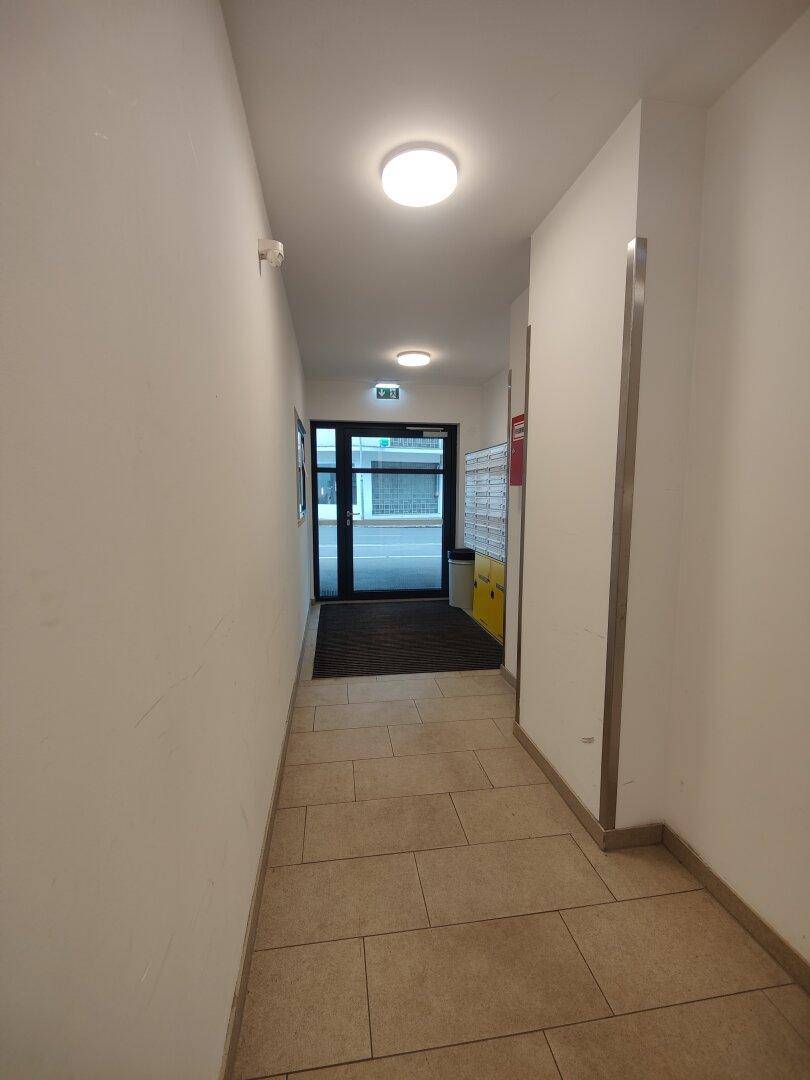 Langer, heller Flur mit Fliesenboden und Blick auf den Gebäudeeingang.