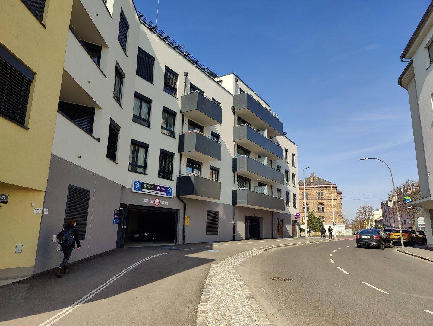 Modernes Wohngebäude mit Tiefgarageneinfahrt und Balkonen an einer Straße.