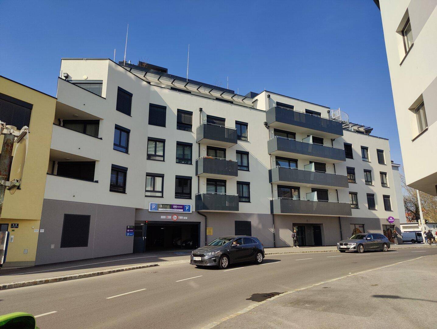 Neues Wohngebäude mit moderner Architektur, Balkonen und Tiefgaragenzugang.