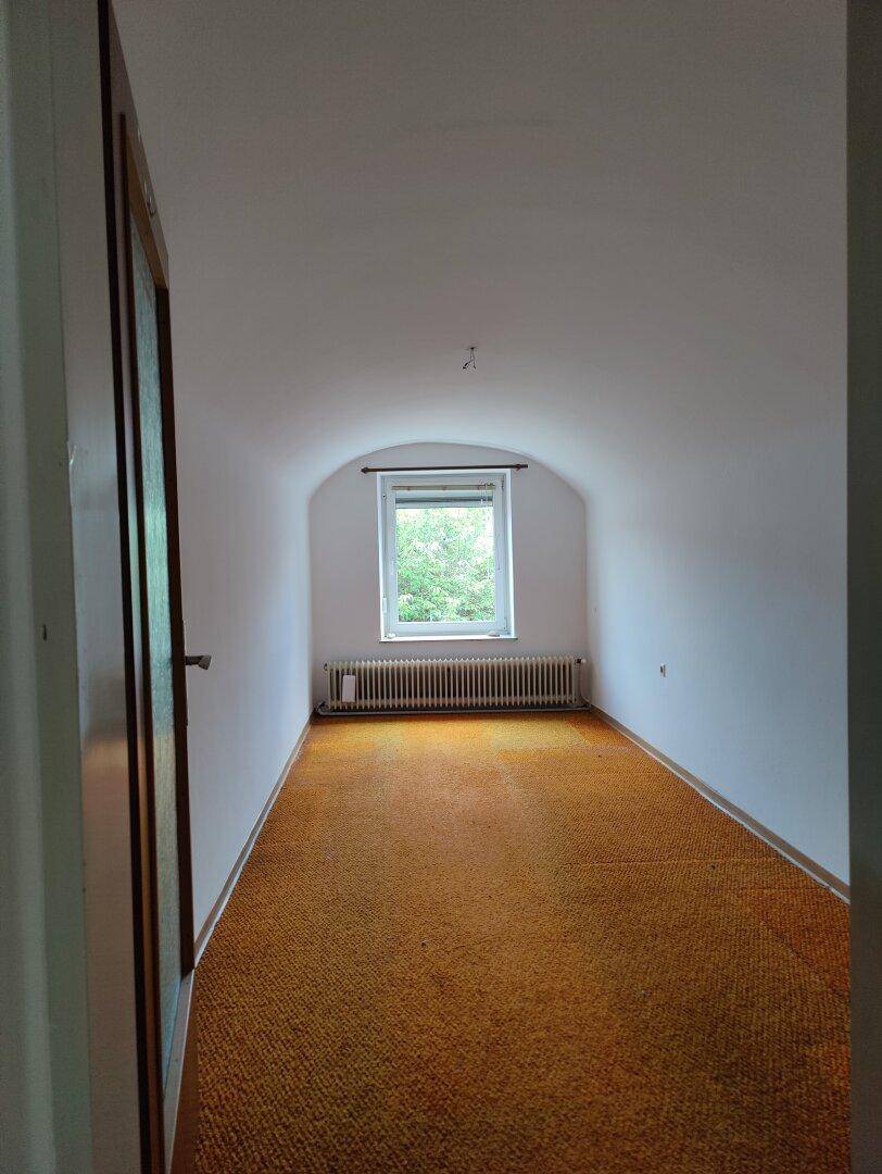 Schmaler Raum mit Teppichboden und einem Fenster, das eine grüne Aussicht bietet.
