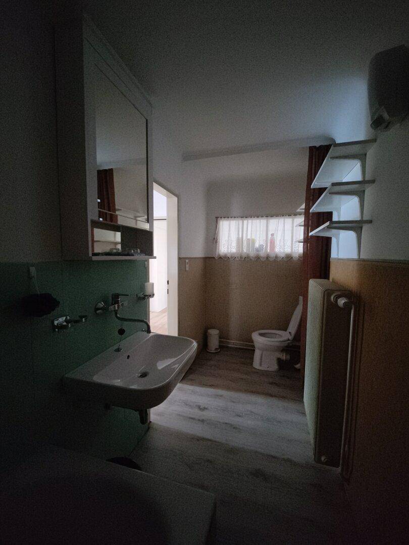 Dunkles Badezimmer mit Waschbecken, Toilette und einfacher Ausstattung.