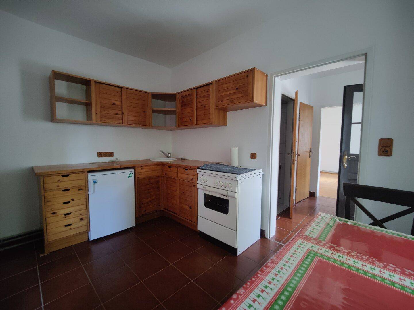 Funktionale Küche mit Holzschränken, Fliesenboden und Platz für einen Esstisch.