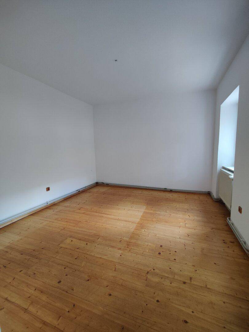 Heller, leerer Raum mit breiten Holzplanken und weißen Wänden.