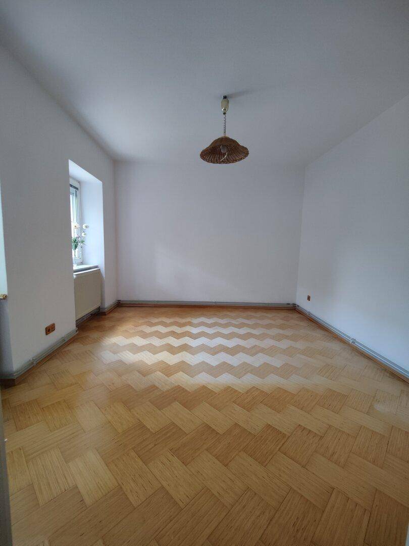 Geräumiger Raum mit hellem Fischgrätparkett und einem Fenster für natürliche Belichtung.