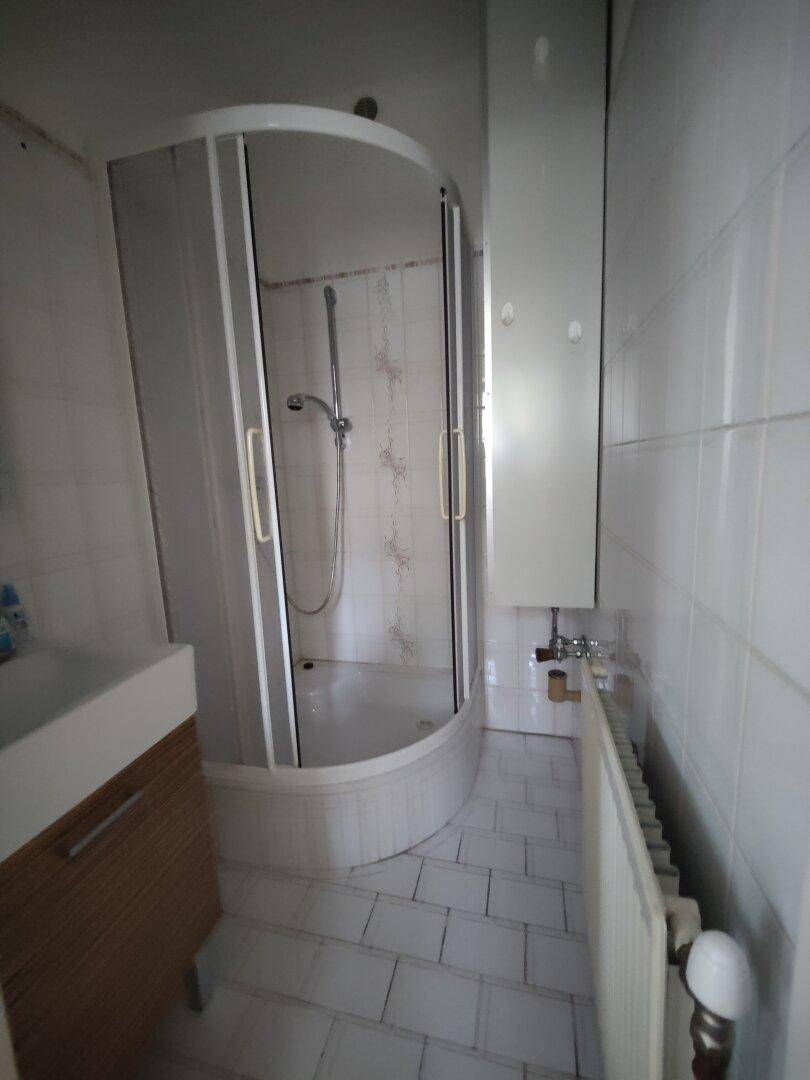 Kleines Badezimmer mit Duschkabine, weißen Fliesen und Heizkörper.