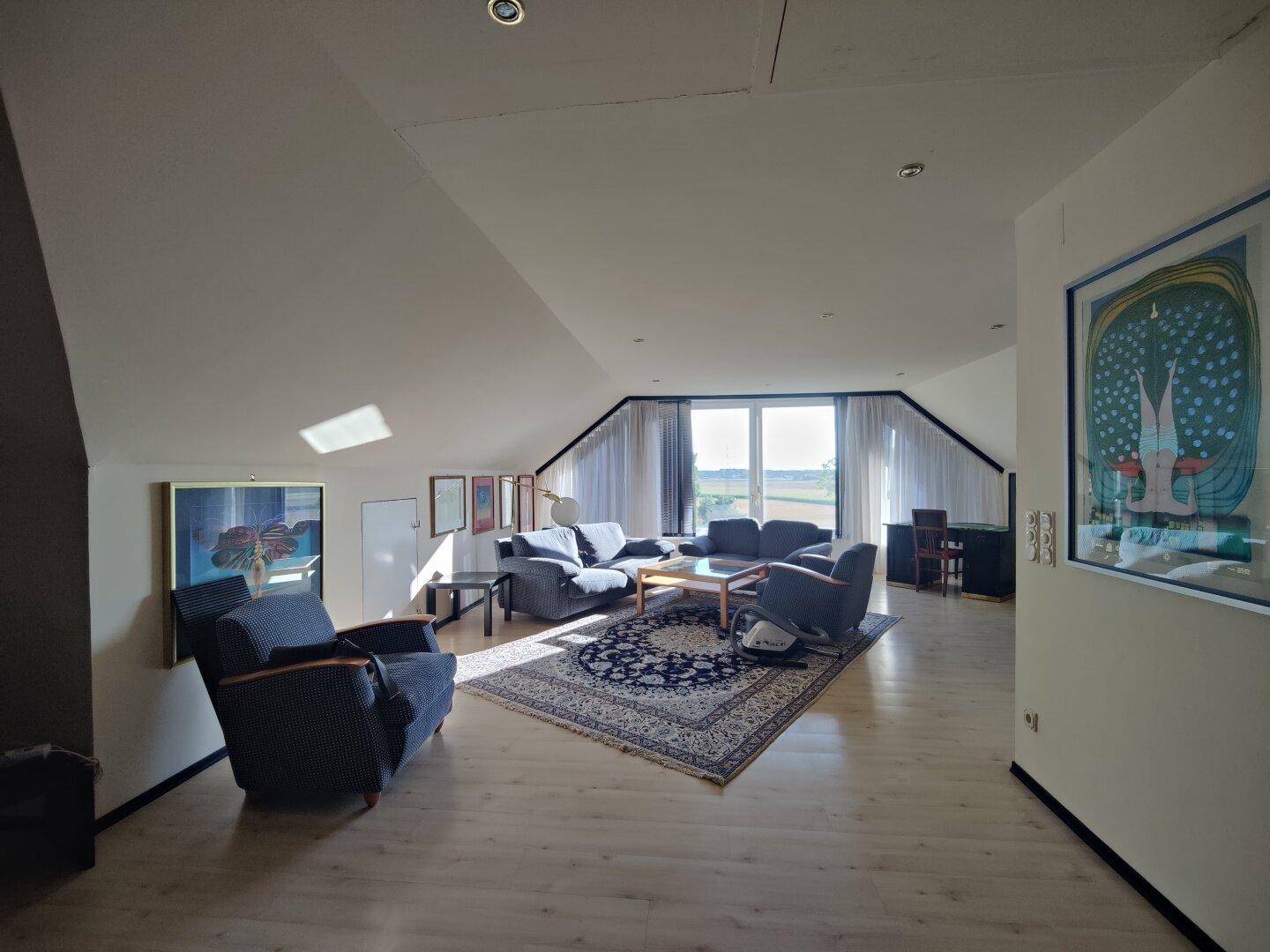 Lichtdurchfluteter Wohnbereich im Dachgeschoss mit Panoramablick durch große Fenster.