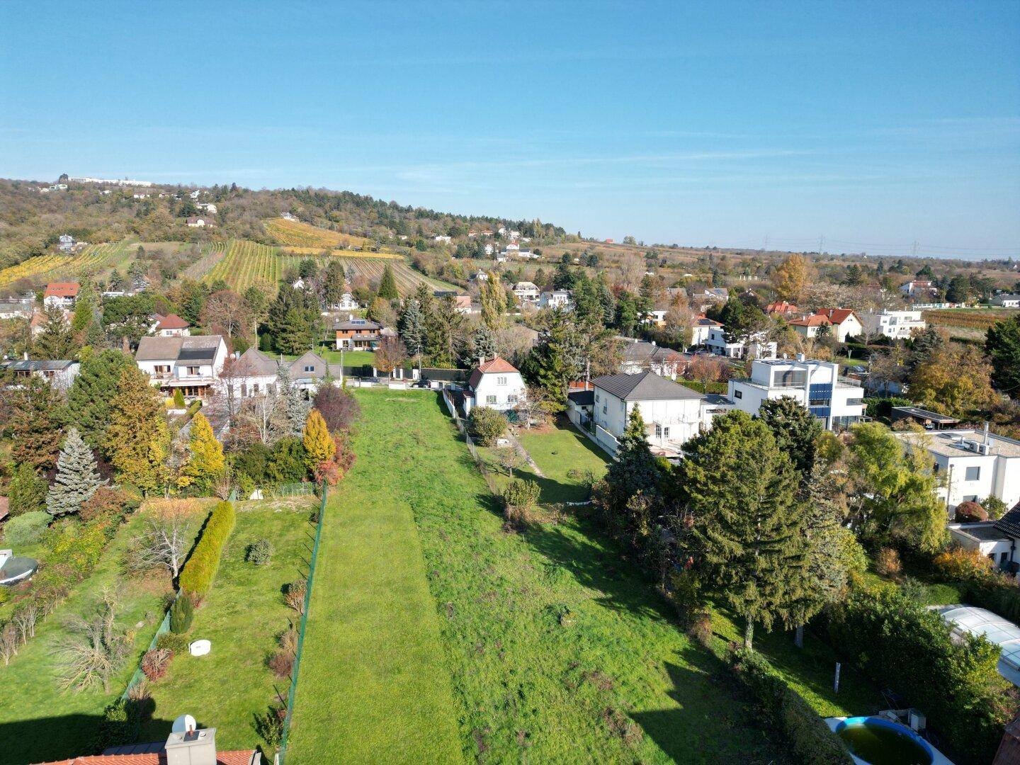 Panoramablick über eine Wohngegend mit Weinbergen im Hintergrund unter blauem Himmel.